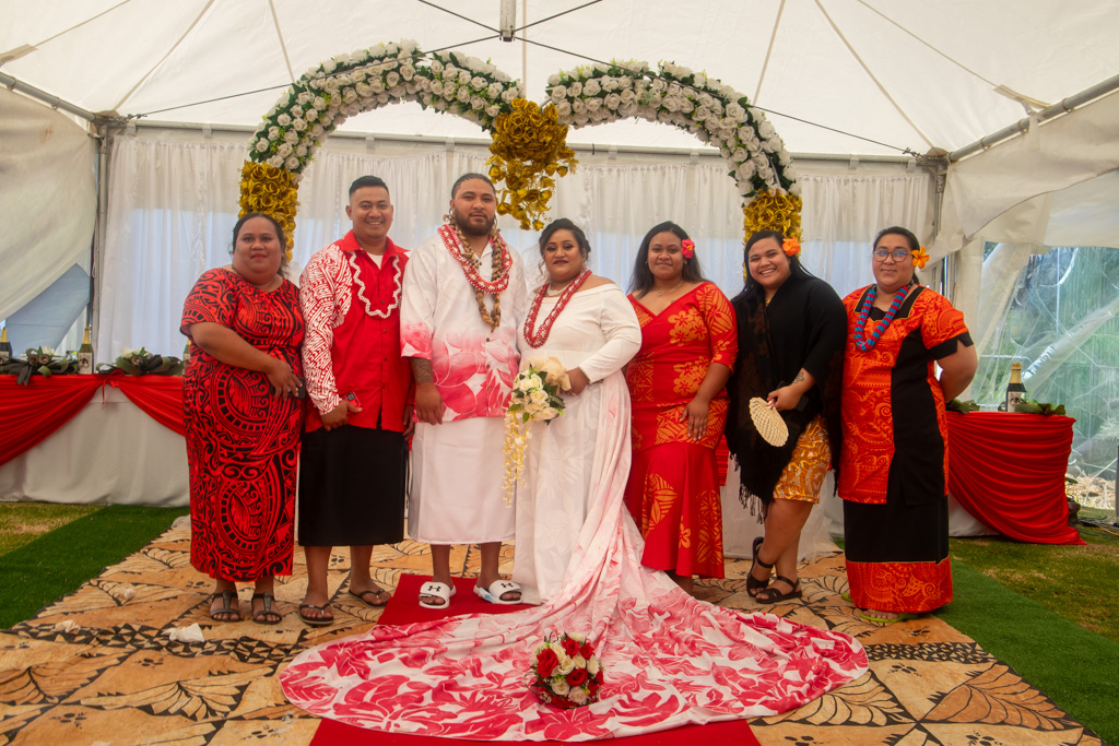 Auckland wedding photographer — Pacific wedding couple with family under floral arch